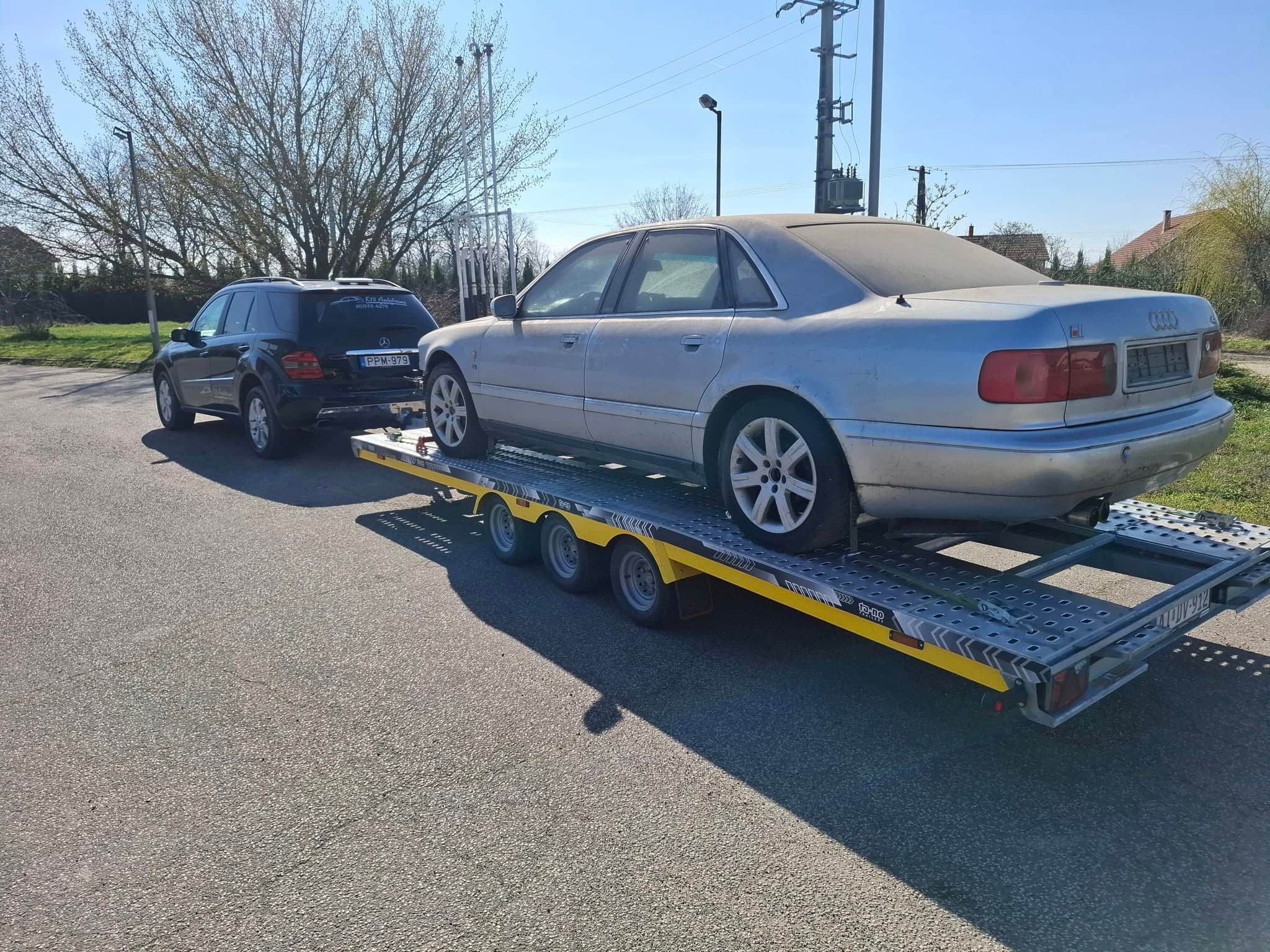 Ezüst Audi A8 tréleren, autószállítás közben az út szélén